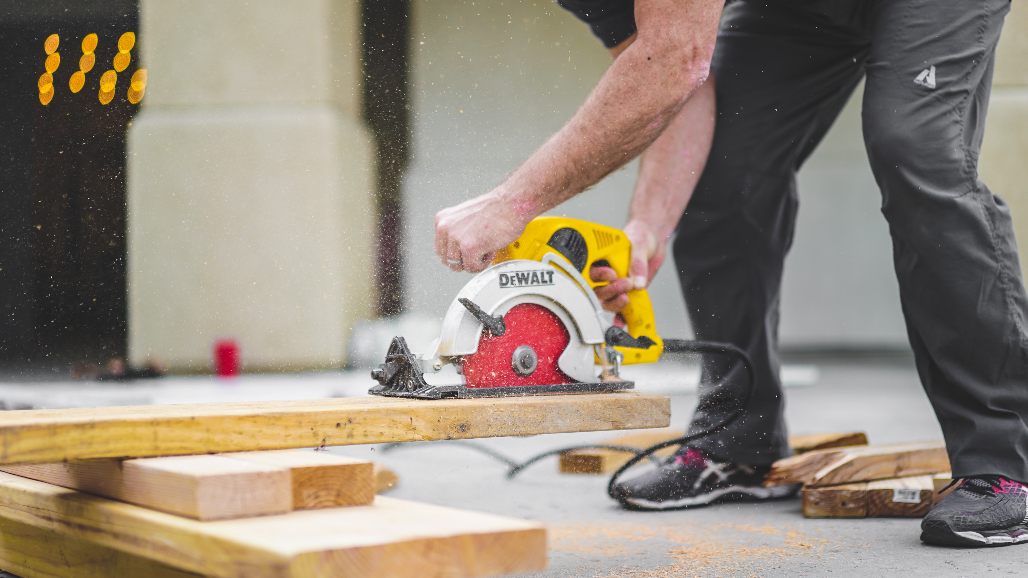 Person holding a hand saw cutting a 2x4 with sawdust flying from the blade