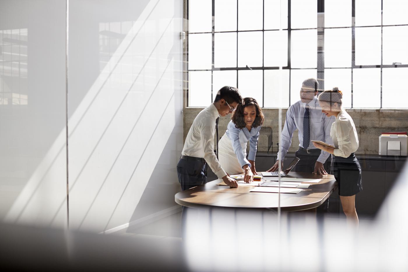 Group of young professionals around a table discussing paperwork in a bright office with lots of windows